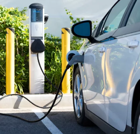 Voiture électrique blanche branchée à une borne, avec le câble de recharge au premier plan.