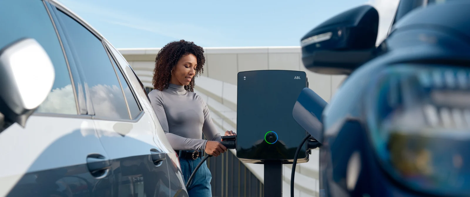 Borne Wallbox ABL eM4 installée entre deux places de parking, avec une utilisatrice