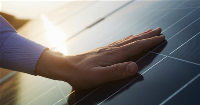 Une main posée sur un panneau photovoltaïque éclairé par le soleil