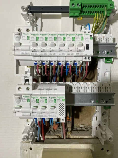 Tableau électrique ouvert sur un mur blanc montrant les rangées de disjoncteurs