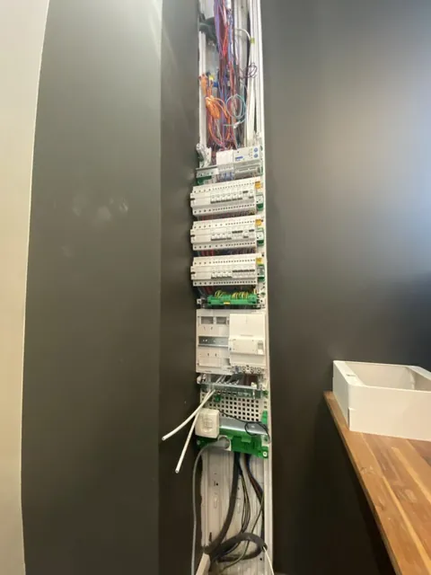 Tableau électrique vertical ouvert près d’un mur gris et d’un plan en bois