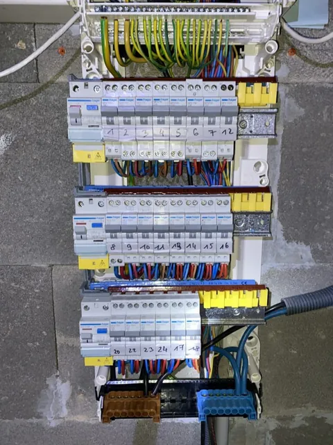 Grand tableau électrique ouvert avec ses étiquettes de repérage jaunes et ses conduits