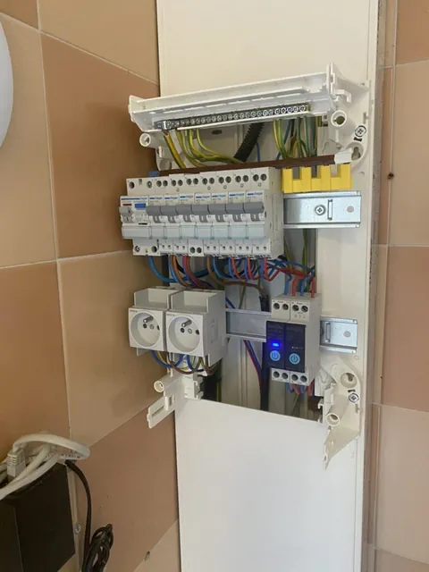 Petit tableau électrique sur un panneau de bois raccordé par des conduits blancs