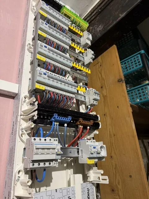 Tableau électrique ouvert avec ses rangées de disjoncteurs et ses conducteurs sur un support en bois