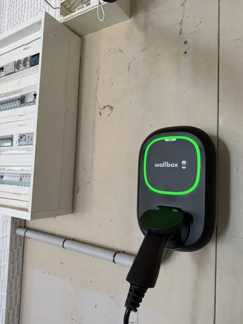 Borne Wallbox au voyant vert avec son câble de recharge raccordé sur un mur blanc