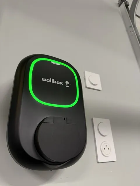 Borne Wallbox au voyant vert installée sur un mur blanc à côté de deux prises
