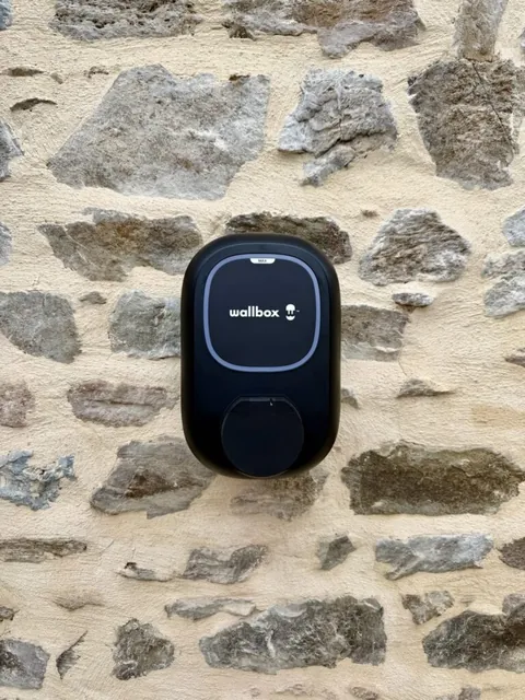 Borne Wallbox au voyant bleu fixée sur un mur en pierre
