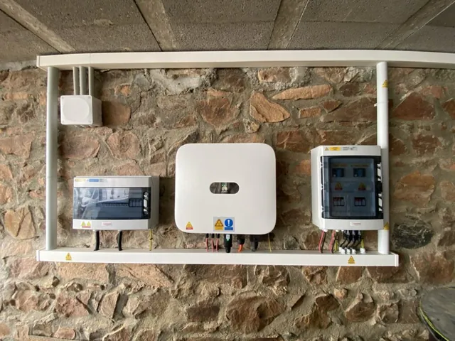 Onduleur mural et coffrets de protection reliés par des conduits sur un mur en pierre