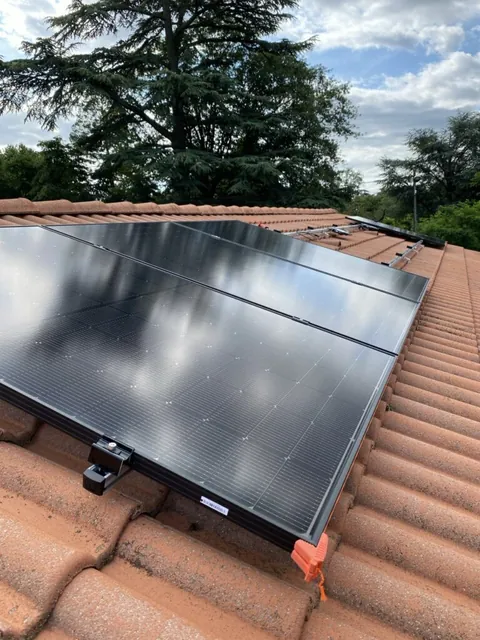 Détail du bord des panneaux photovoltaïques et de leur fixation au-dessus des tuiles rouges