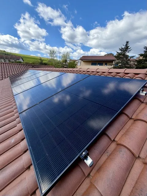 Panneaux photovoltaïques noirs sur une toiture en tuiles rouges, sous un ciel bleu