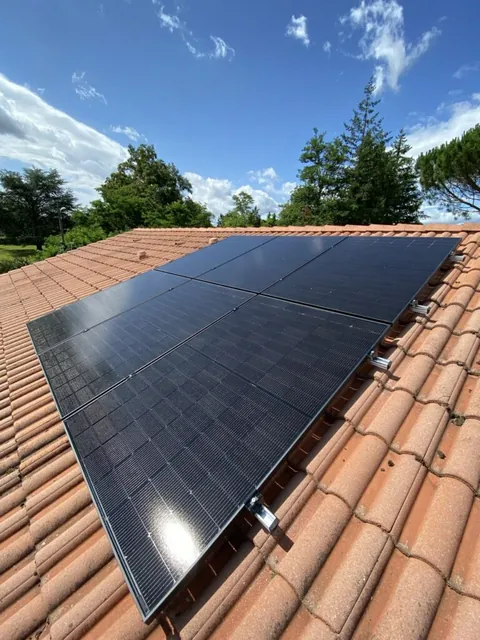 Champ photovoltaïque sur une toiture en tuiles rouges bordée d’arbres